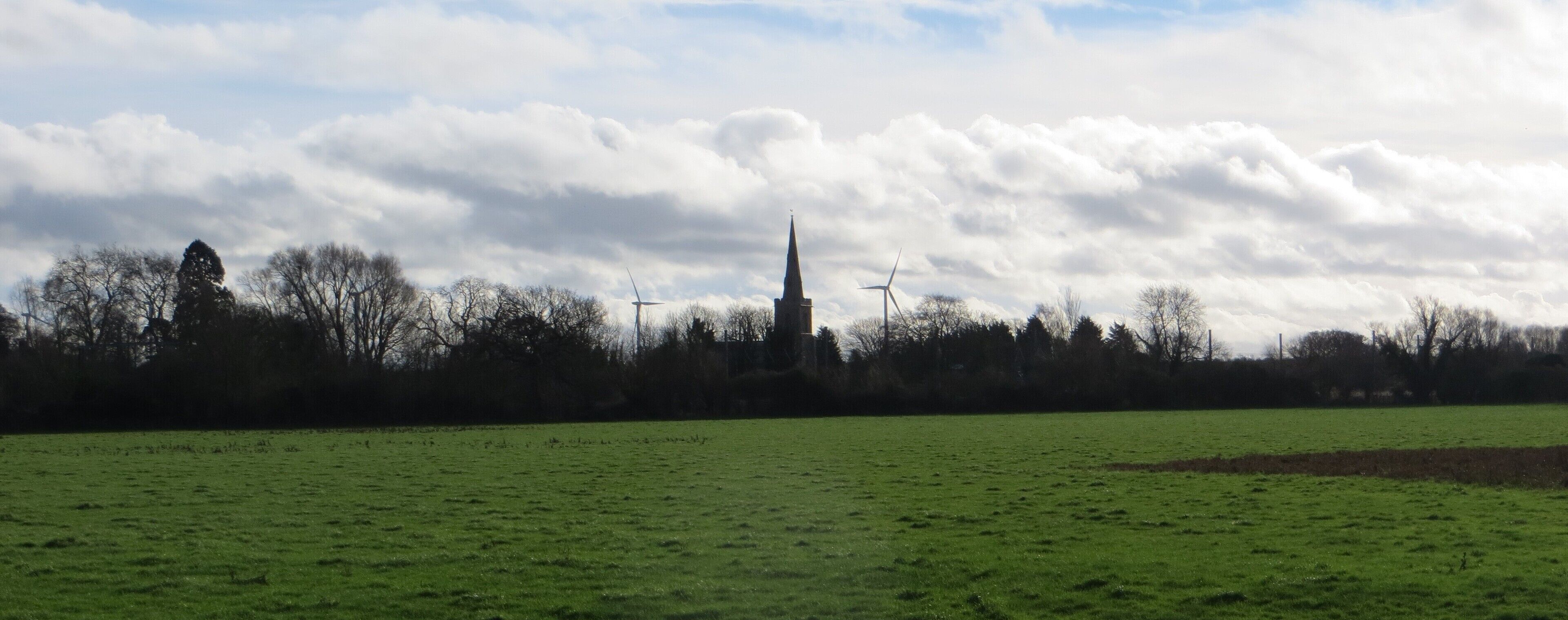 A green field, a church spire, and wind turbines.
