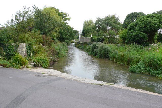A narrow waterway bordered by lush greenery and a paved road.