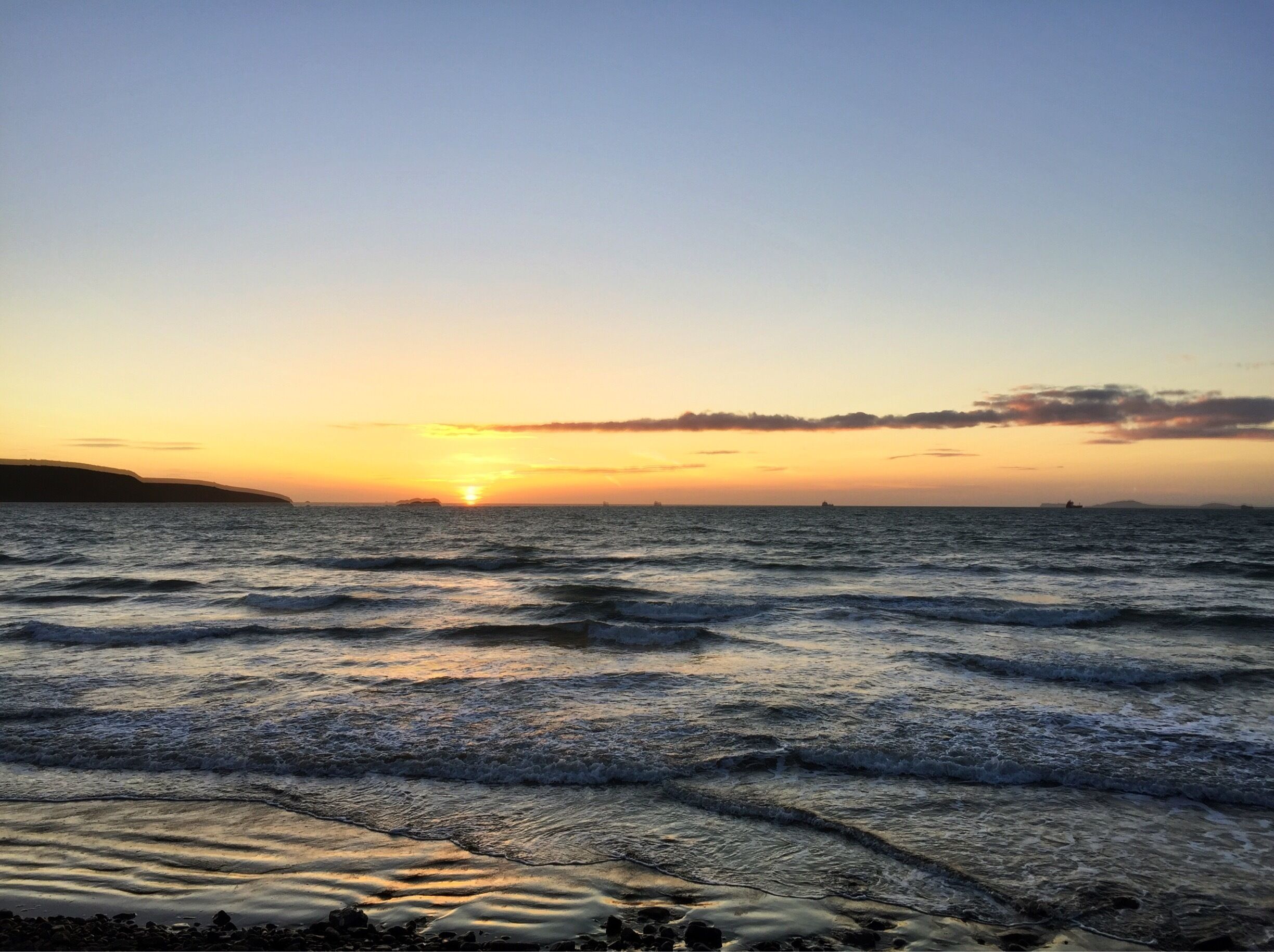 A sunset over the ocean with waves on the shore.