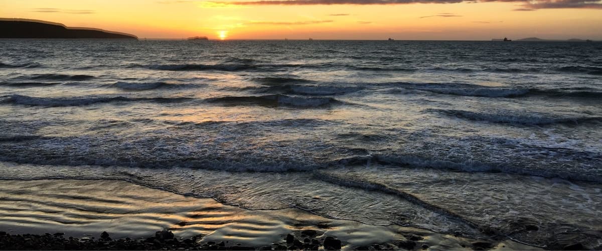 A sunset over the ocean with waves on the shore.