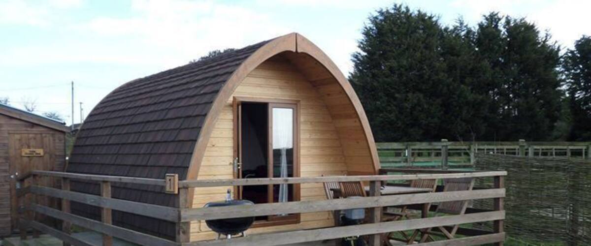 A wooden cabin with a curved roof, a porch, and a grill outside.
