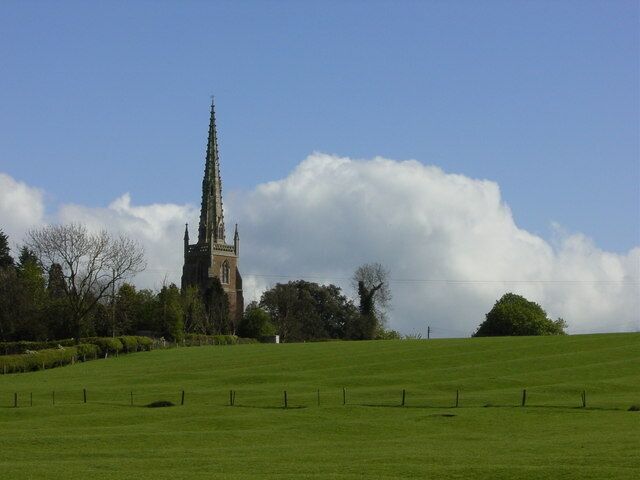 A church with a tall spire, surrounded by a green field and trees.