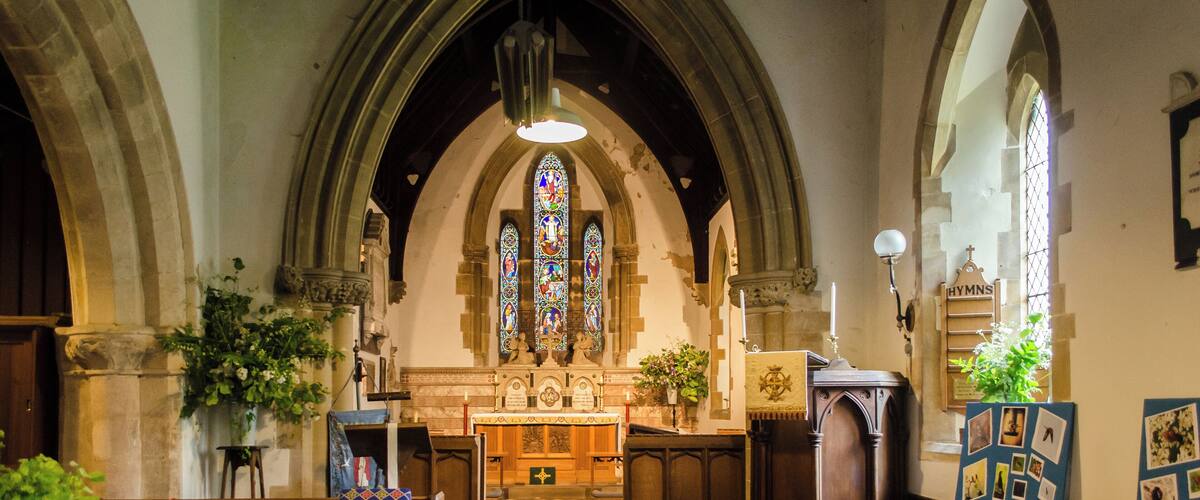 A church interior with wooden pews, stained glass windows, and a central altar.