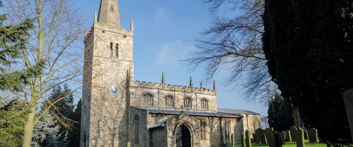A stone church with a tall tower and a red pathway leading to the entrance.