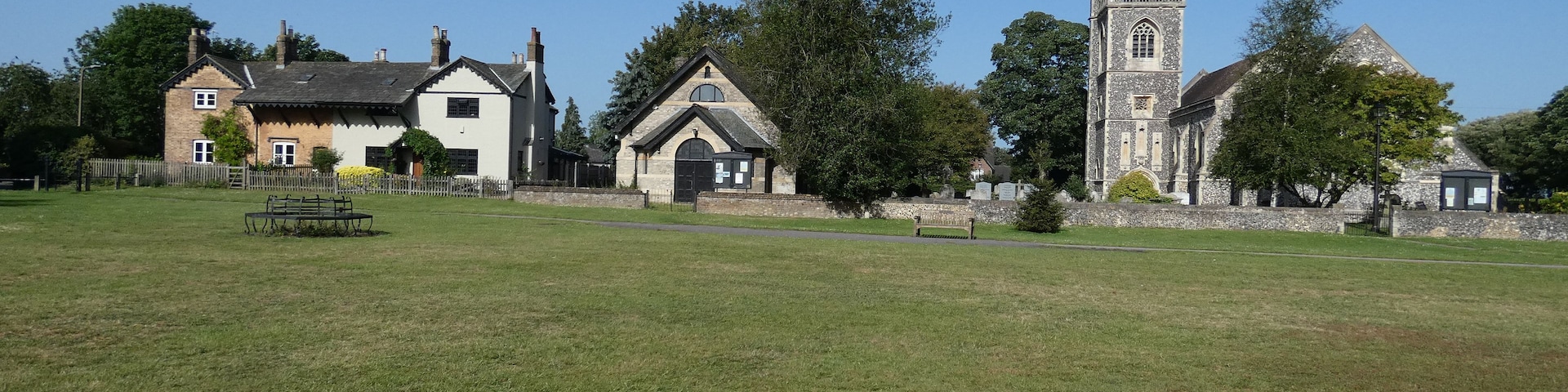 A grassy field with a stone church, a white house, and a wooden bench.