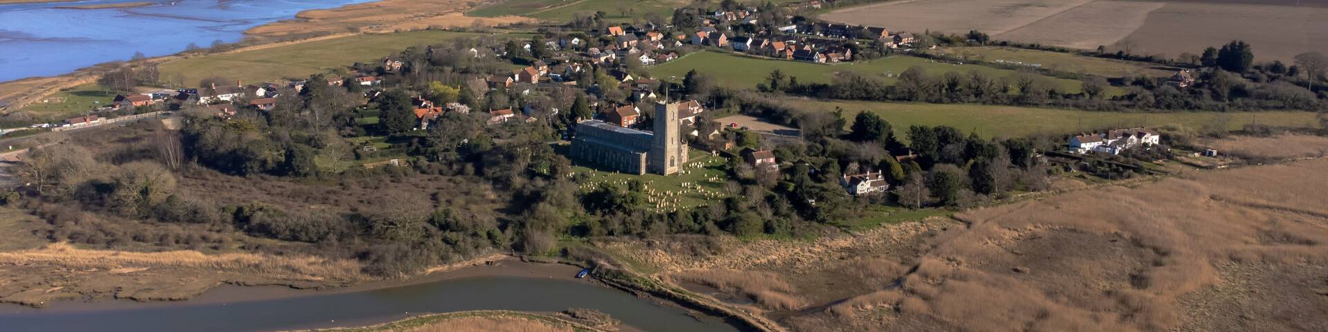 A rural landscape with a river, fields, and a small village with a prominent church.