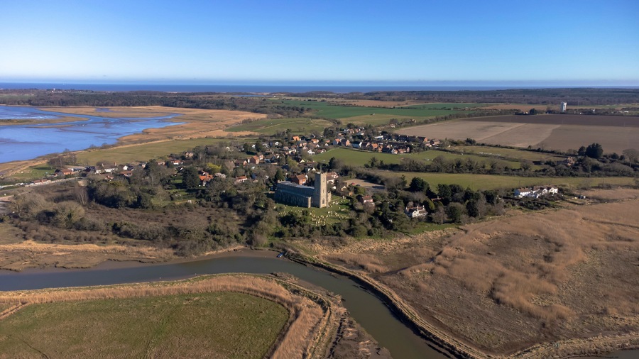 A rural landscape with a river, fields, and a small village with a prominent church.