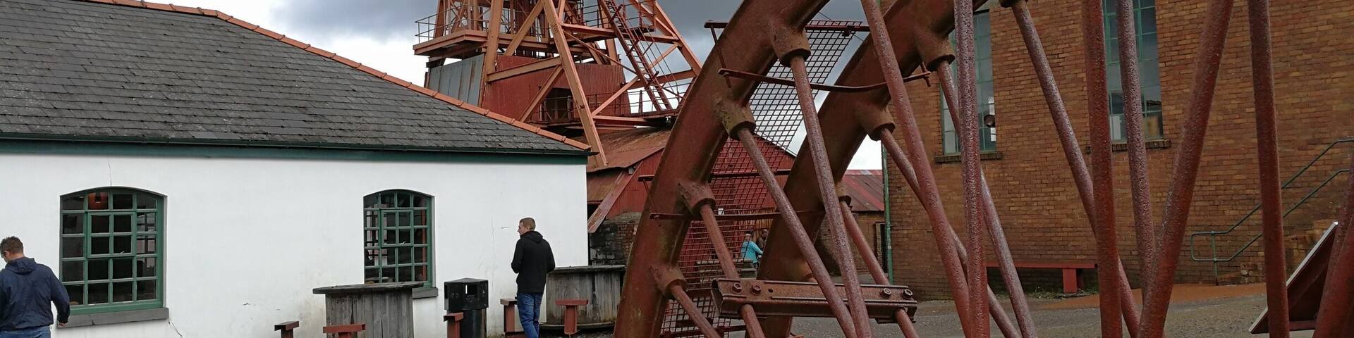 A historical water wheel and a tall tower with a flag, set against a cloudy sky.