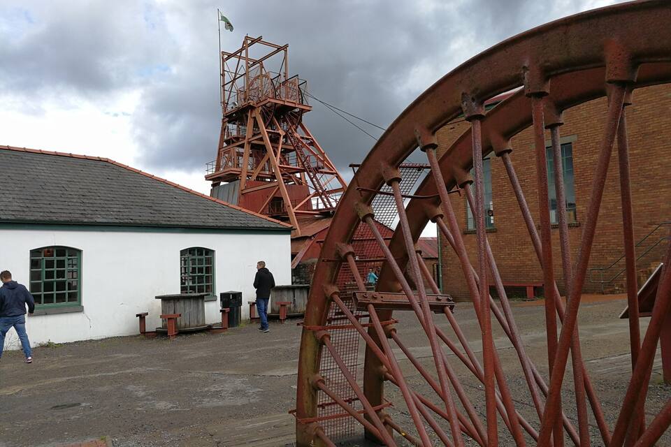 A historical water wheel and a tall tower with a flag, set against a cloudy sky.