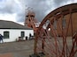 A historical water wheel and a tall tower with a flag, set against a cloudy sky.