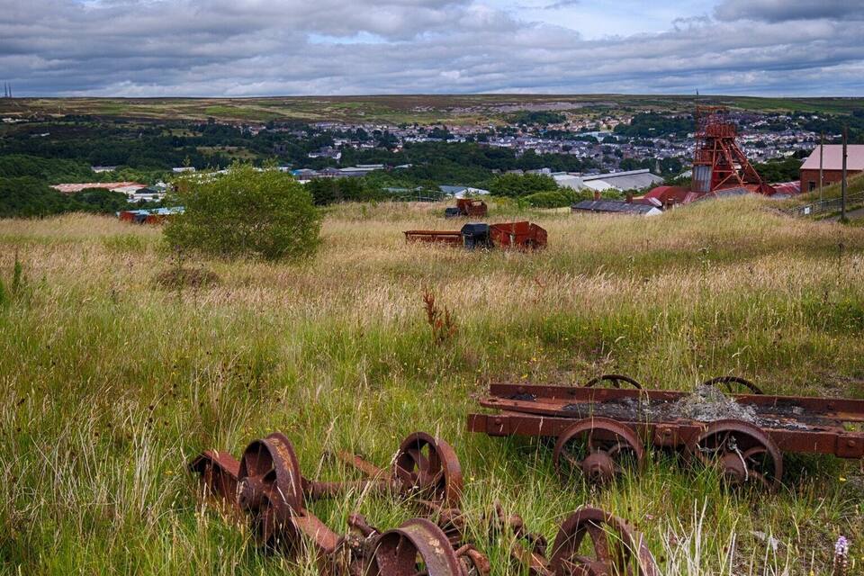 En græsmark med rustne metalgenstande og en fjern minebygning.