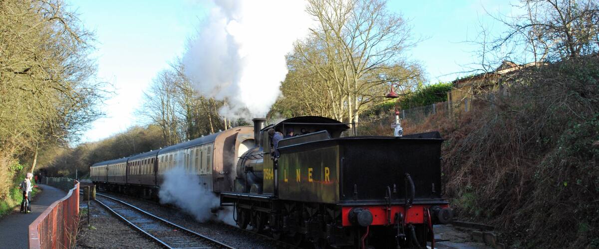 A steam locomotive with the number 7649 on a railway track surrounded by trees and a clear sky.