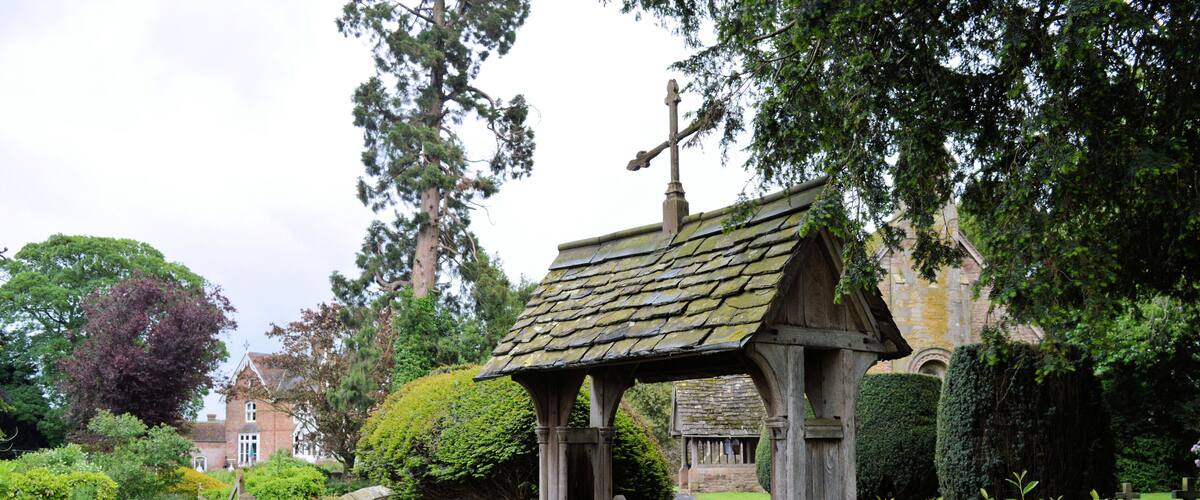 A stone gate with a wooden fence, a stone wall, and a small wooden structure with a tiled roof.