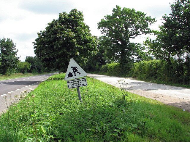 Road materials stored on the highway Announces the sign placed on the grassy strip that separates the A1067 (Norwich Road, seen at left) from an obsolete section of old road at right, by the junction with Stone Lane. The view is southerly.