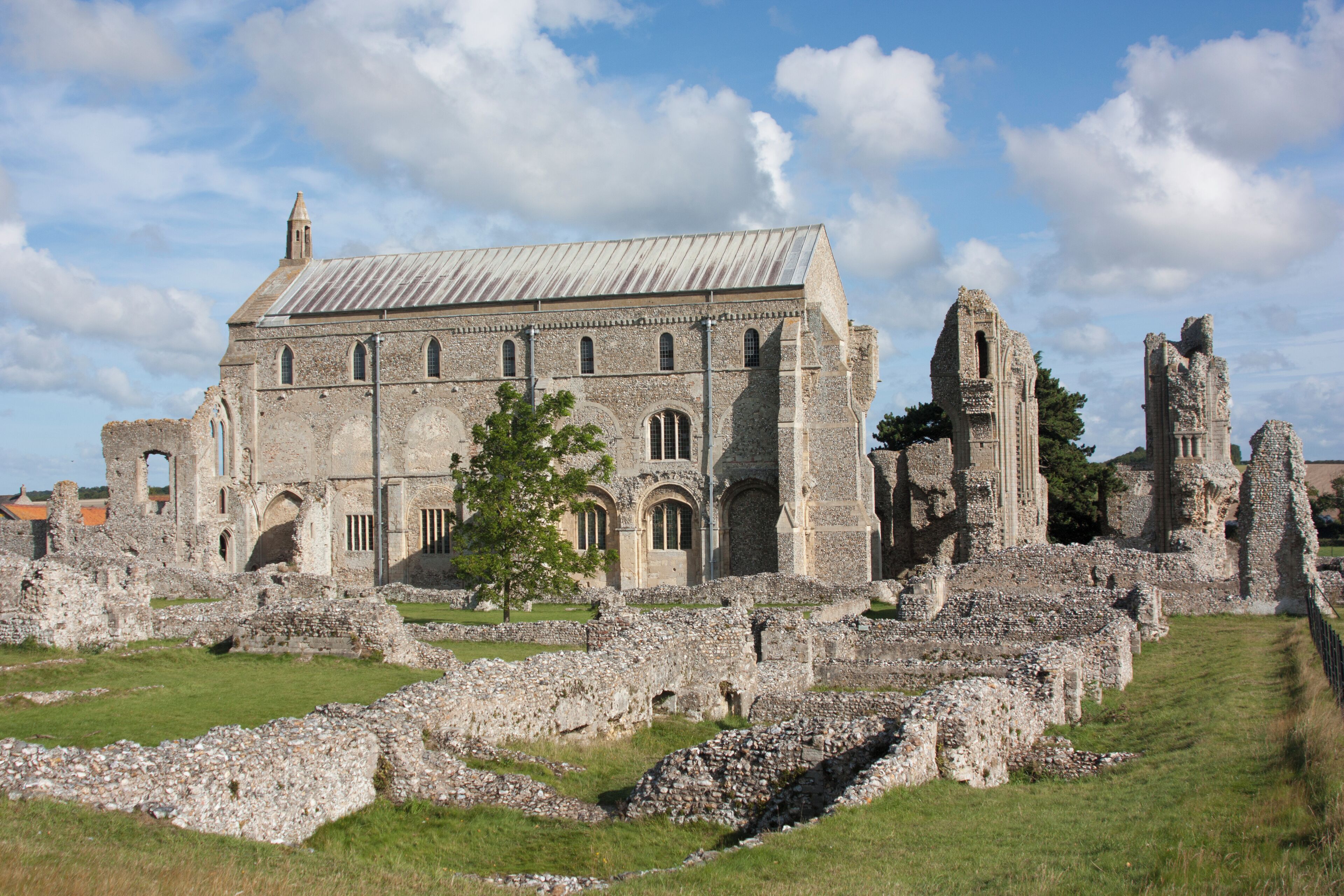 A historic stone building with ruins and a tree in the foreground.
