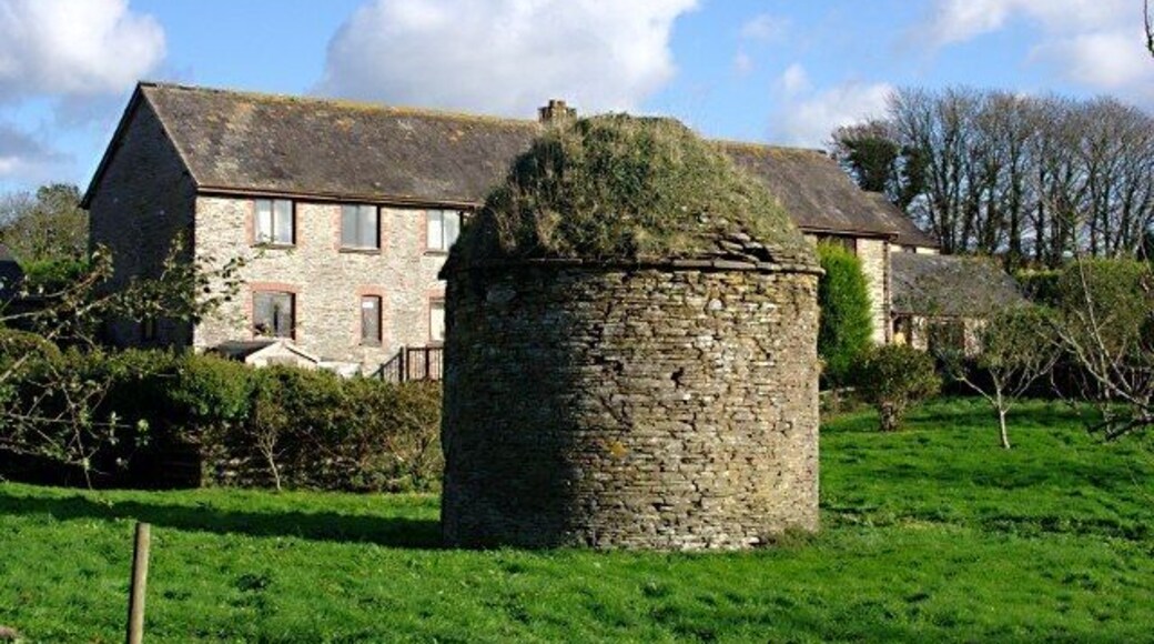 The Dovecote, Bigbury Court, Bigbury, Devon. An old dovecote with rounded roof sits in a field in front of a barn converted to holiday accommodation.
