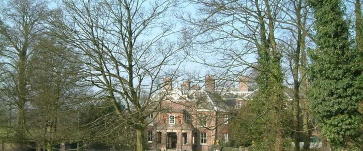 A large brick building with a central entrance, surrounded by trees and a grassy field.
