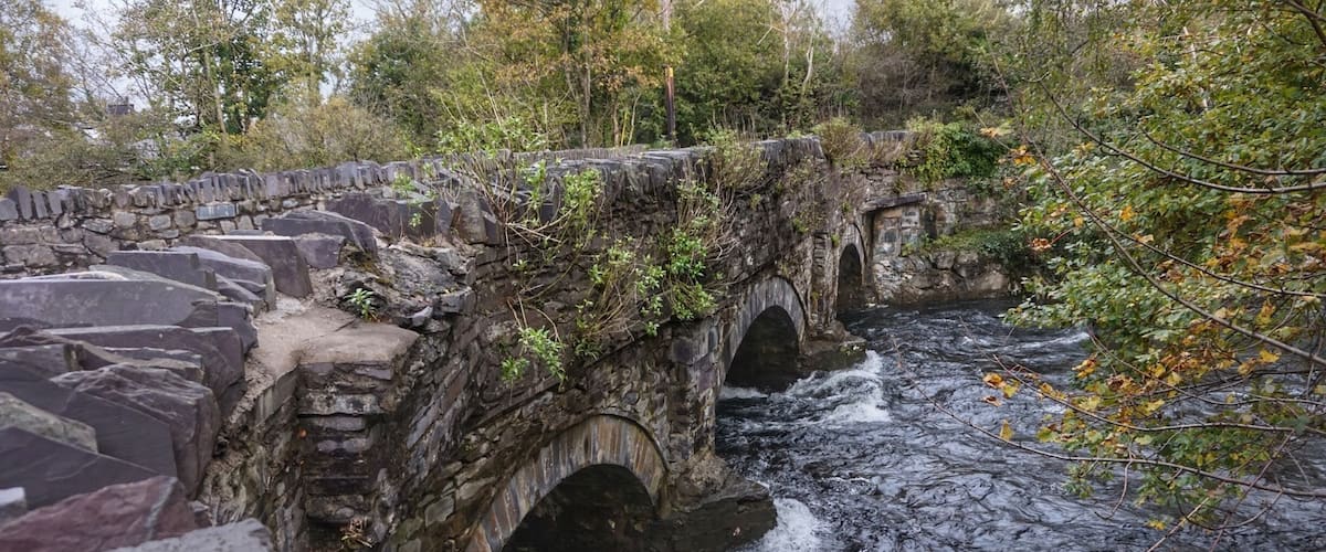 A stone bridge over a flowing river surrounded by trees.