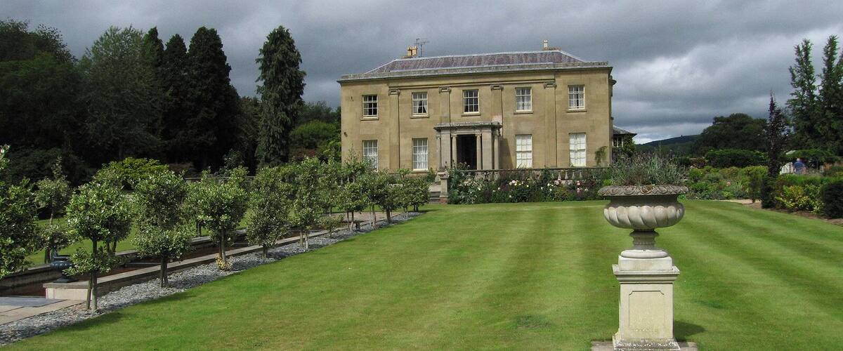 A large, classical building with a symmetrical facade, surrounded by a well-manicured lawn and rows of trees.