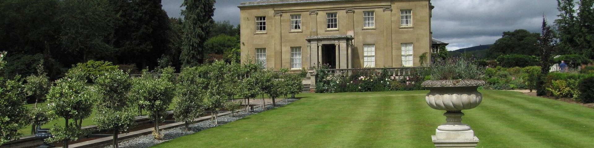 A large, classical building with a symmetrical facade, surrounded by a well-manicured lawn and rows of trees.