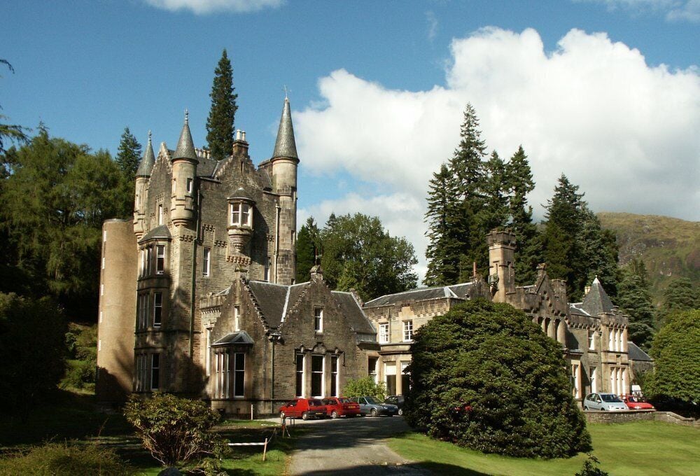 A historic castle with multiple towers, surrounded by lush greenery and a clear sky.