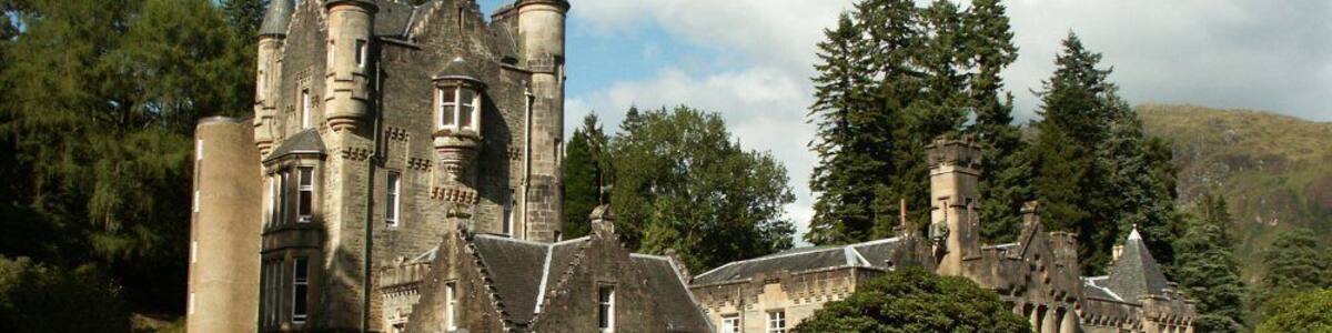 A historic castle with multiple towers, surrounded by lush greenery and a clear sky.