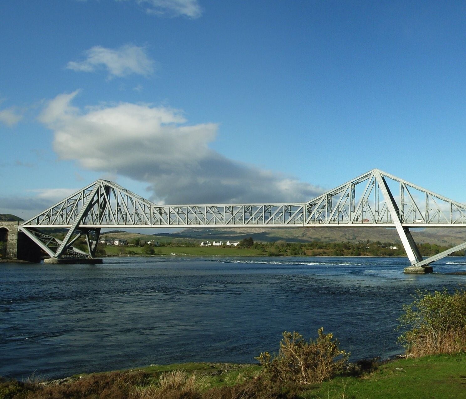 A steel truss bridge over a river with a clear sky.