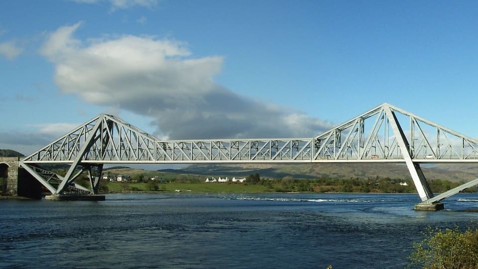 A steel truss bridge over a river with a clear sky.