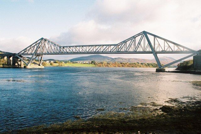 A steel truss bridge over a river with mountains in the background.