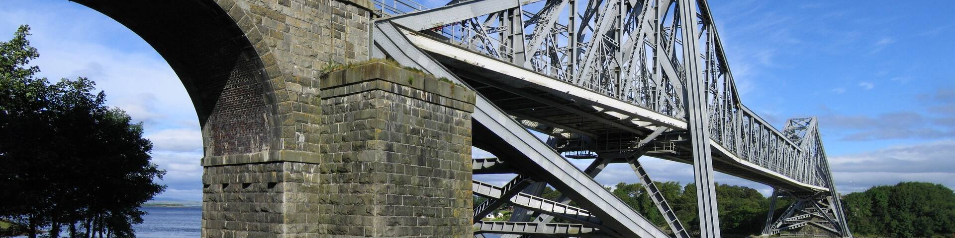 A stone bridge with a metal truss structure spanning a river.