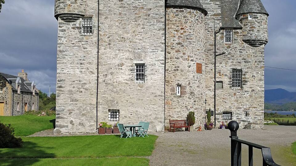 A stone castle with multiple towers and a well-maintained lawn.