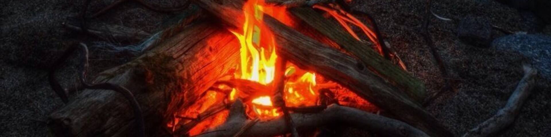 A campfire at dusk with a sunset over rocky terrain.