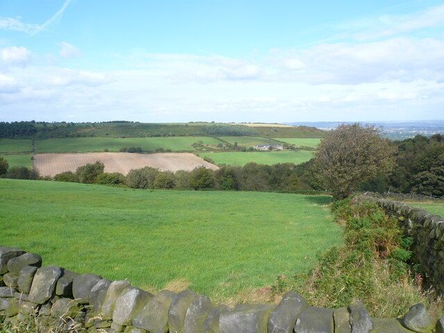 A rural landscape with a stone wall, green fields, and distant hills.