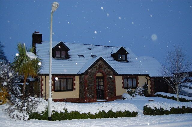 A snow-covered house with a brick facade, a peaked roof, and a front porch.