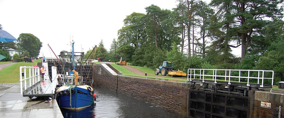 A canal with a boat docked on the left, a lock gate, and a tractor on the right.