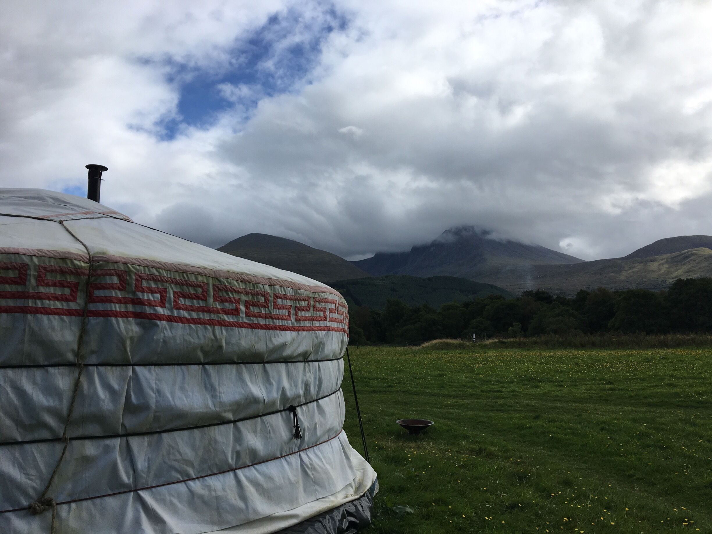 A large tent in a grassy field with mountains in the background.
