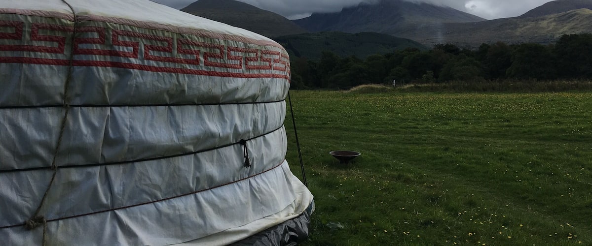 A large tent in a grassy field with mountains in the background.