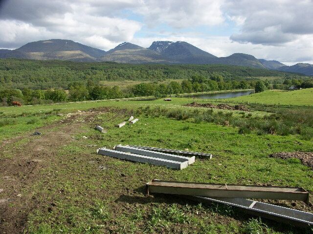A rural landscape with a river, mountains, and scattered concrete structures.