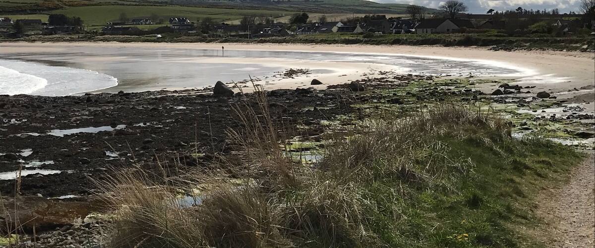 A coastal landscape with a sandy beach, rocky shore, and a village in the background.