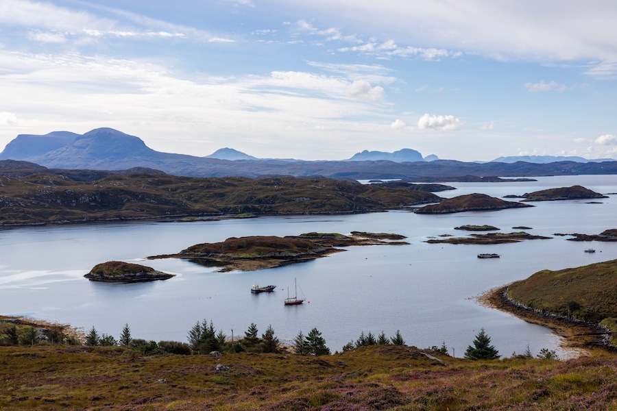 A coastal landscape with a large body of water, several small islands, and distant mountains under a partly cloudy sky.