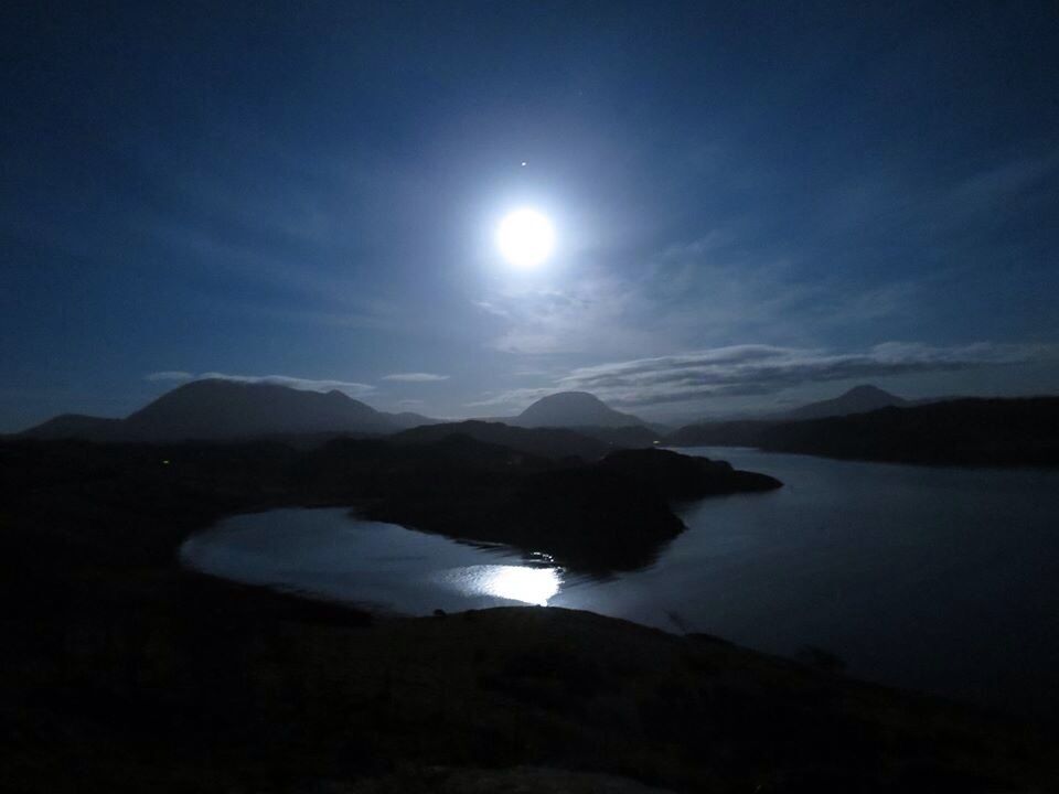 A night landscape with a bright moon, a lake, and mountains.