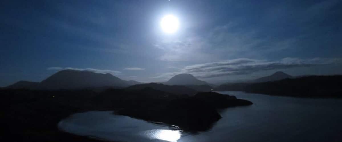 A night landscape with a bright moon, a lake, and mountains.