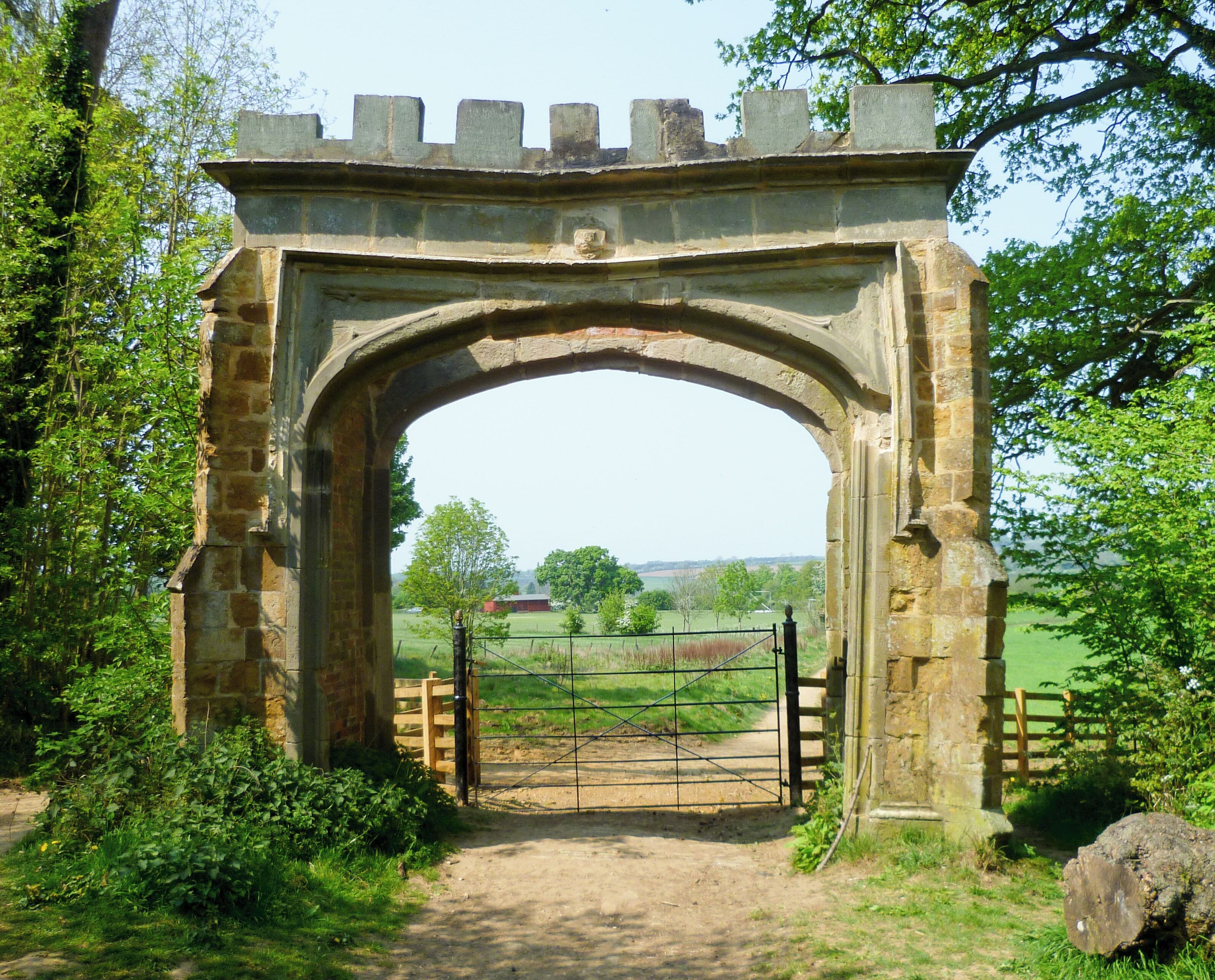 An old stone archway with a gate, surrounded by greenery and trees.