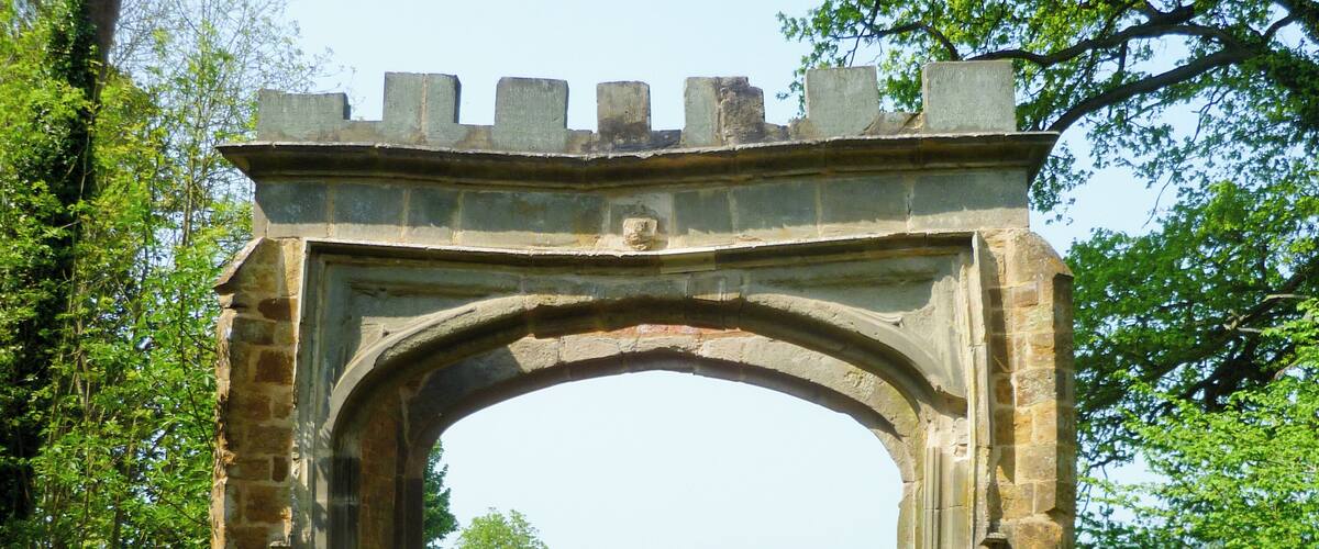 An old stone archway with a gate, surrounded by greenery and trees.