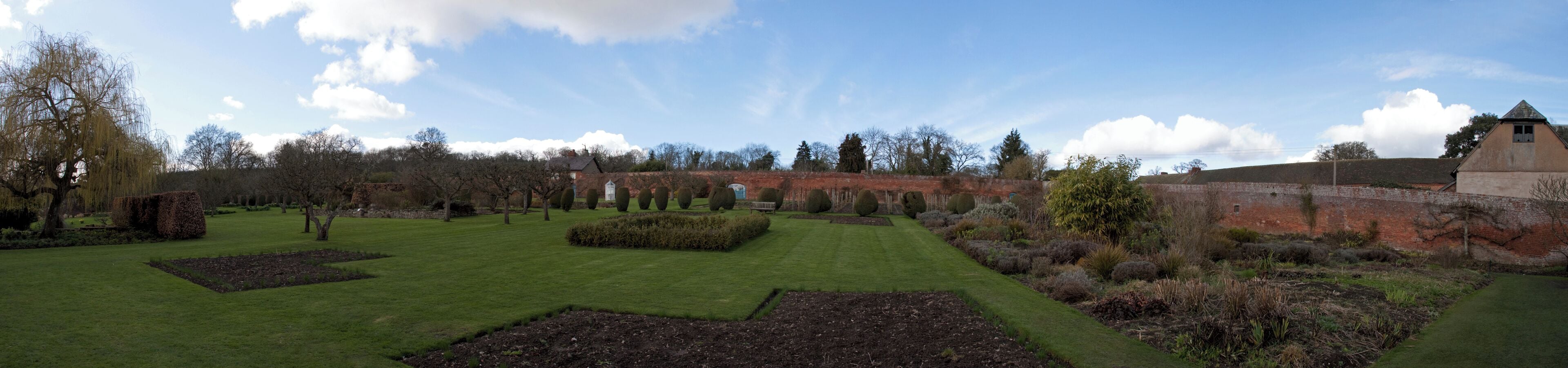 A landscaped garden with manicured lawns, hedges, and a brick wall.
