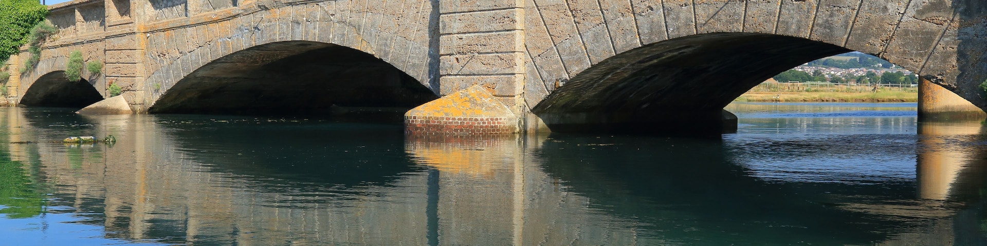 Un puente de piedra con tres arcos sobre un río tranquilo.