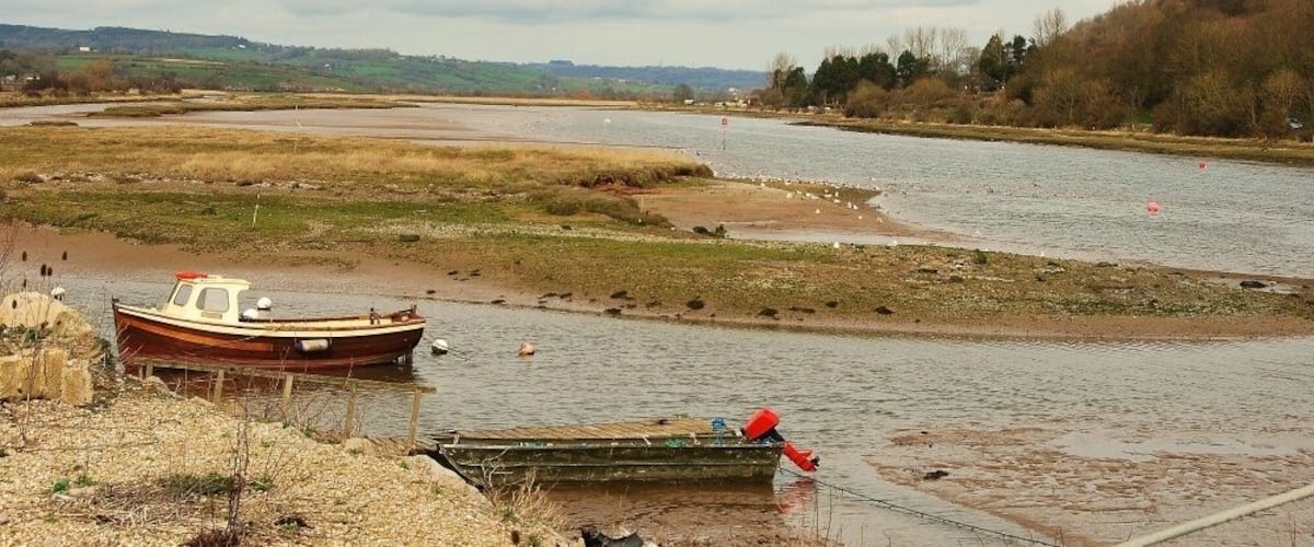 A river with boats, a grassy bank, and distant hills.