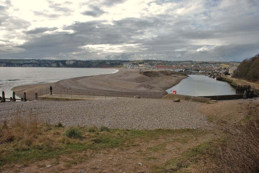 Seaton: River Axe and sea Picture shows the Rixer Axe, on the right, flowing parallel to the sea shore, separated by a pebble beach peninsula. A small jetty is visible on the left and Seaton in the distance.