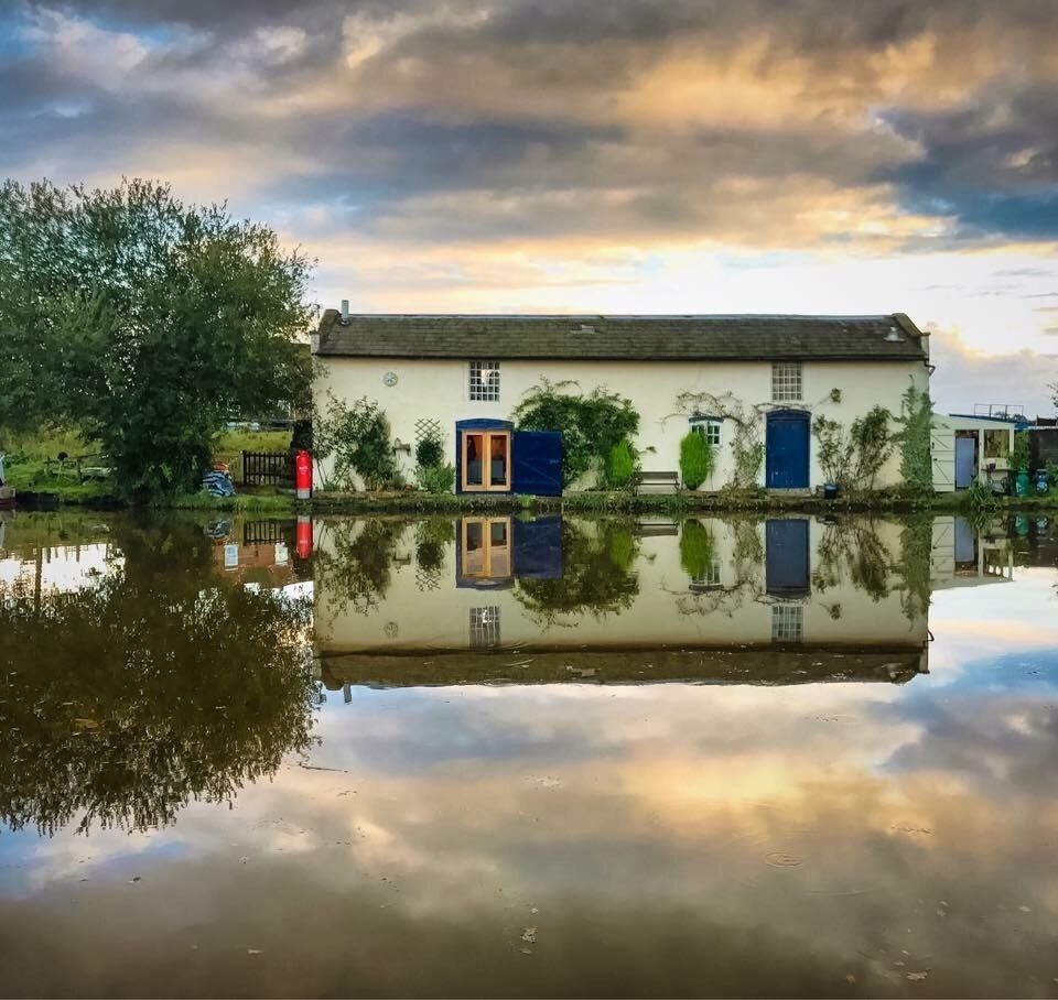 A house with a blue door and windows, reflected in calm water.