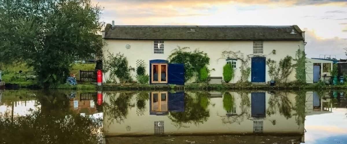 A house with a blue door and windows, reflected in calm water.